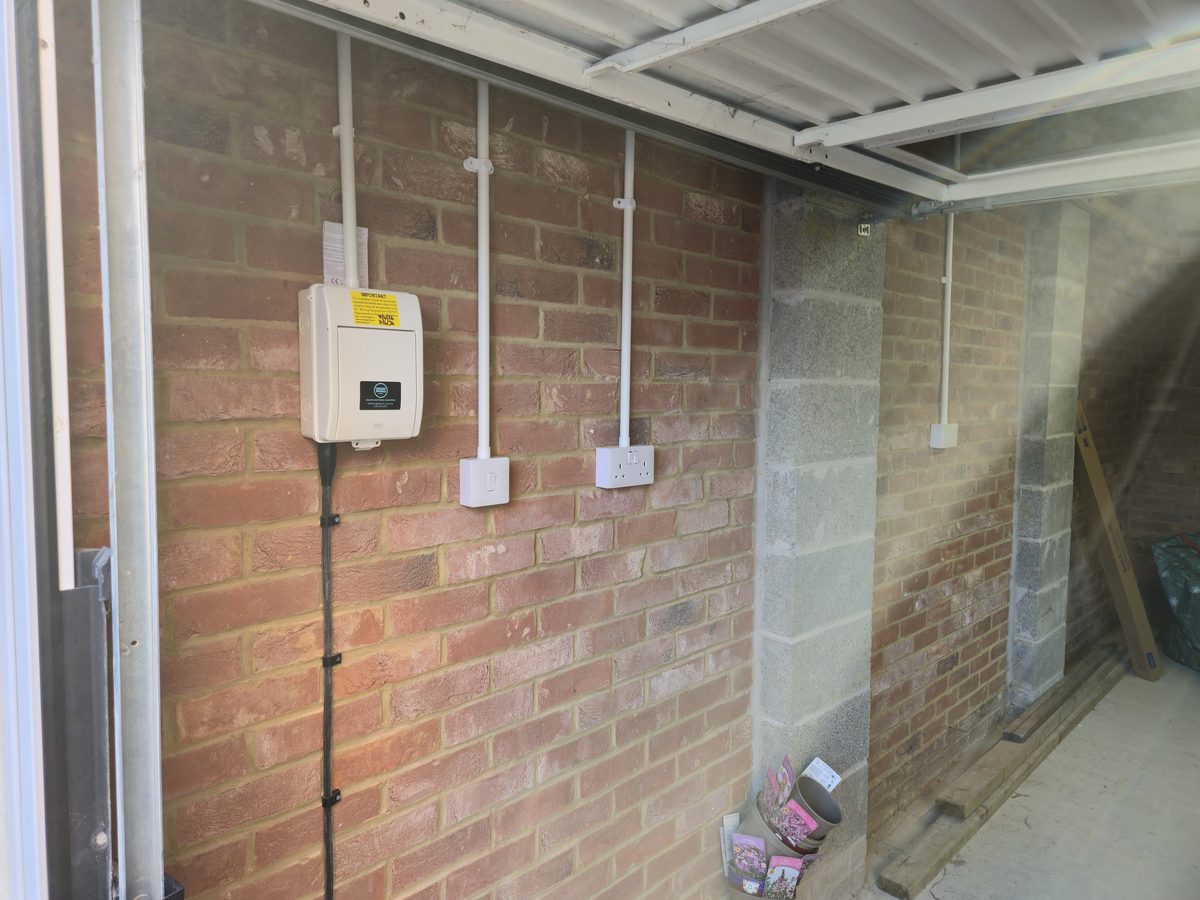 Finished garage installation. BG consumer unit, white conduit, light switch and double socket on brick wall
