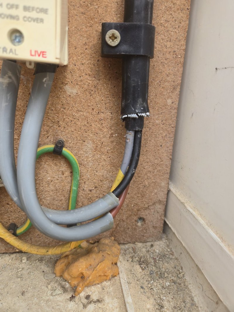 Steel wire armoured sub-main entering a main switch with no gland fitted, the armour over-taped and a core sleeved with salvaged meter-tail sheath.